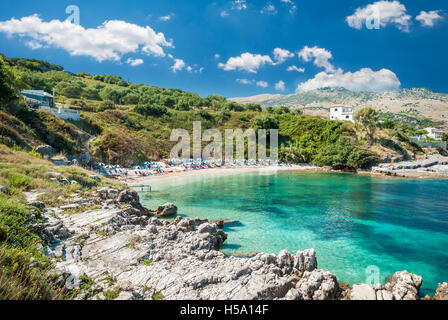 Kassiopi Beach, Korfu, Griechenland. Sonnenliegen und Sonnenschirme (Sonnenschirm) am Strand. Touristen am Strand entspannen. Stockfoto