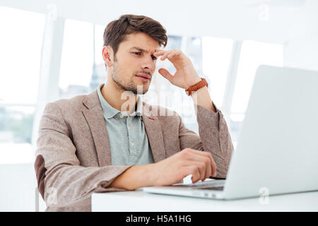 Nachdenklicher junger Geschäftsmann arbeiten mit Laptop im Haus Stockfoto