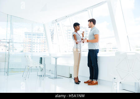 Zwei junge Geschäftsleute stehen und sprechen im Büro während der Kaffeepause Stockfoto