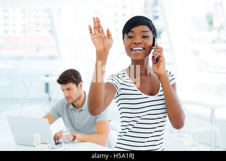 Lächelnde Afro amerikanische Geschäftsfrau winken beim Telefonieren mit Handy im Büro Stockfoto