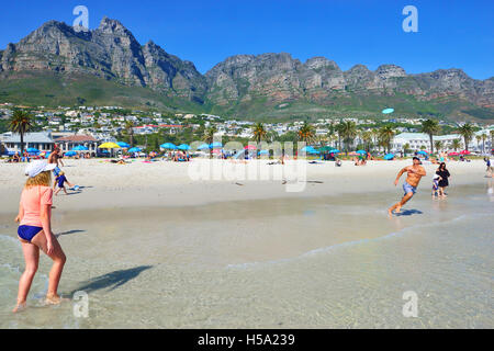 Menschen, die an einem heißen sonnigen Tag am Strand von Camps Bay mit einer Frisbee spielen, einem Strand mit der Blauen Flagge in der wohlhabenden Vorstadt Kapstadt, Südafrika. Stockfoto