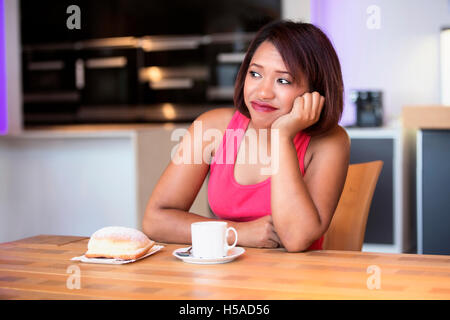 schöne spanische Frau sitzt in der Küche mit Kaffee und Gebäck auf der Suche zu langweilen Stockfoto