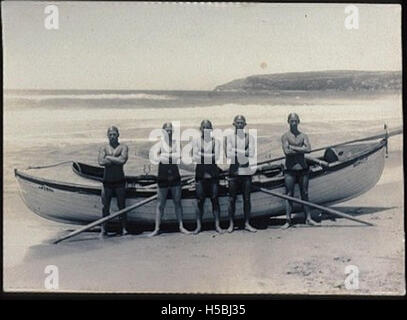 Ein Foto des Surfboots AKUBRA am Strand, begleitet von fünf Mitgliedern des Queenscliff Surf Life Saving Club. Dieses Bild fängt das Strandschwimmer-Team mit seinem surfboat ein und betont die Rolle von Surf-Rettungsclubs für die Sicherheit an der Küste. Stockfoto