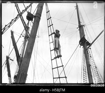 Dieses Foto zeigt eine junge Frau, die auf den Hüllen eines Schiffes steht, wahrscheinlich in der Zeit zwischen 1920 und 1939. Das Bild zeigt die Interaktion der Frau mit der Takelage des Schiffes, ein häufiger Anblick auf Seeschiffen während dieser Zeit. Stockfoto