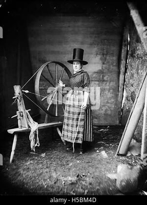 Ein Foto einer Frau in traditioneller walisischer Nationalkleidung, die ein drehendes Rad bedient und walisische Kultur und Handwerkskunst hervorhebt. Stockfoto