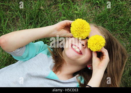 Junges Mädchen mit in grüne Gras spielen mit Blumen über die Augen und lächeln Stockfoto