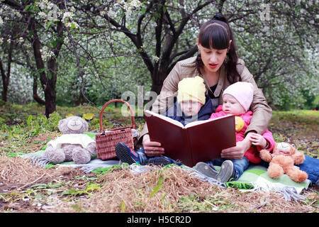 Mutter mit Zwillingen auf Plaid im Freien im Apfelgarten Stockfoto