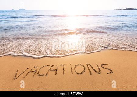 Urlaub in den Sand von einem tropischen Strand mit Sonnenuntergang im Hintergrund geschriebener text Stockfoto