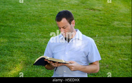 Mann liest die Bibel im Freien auf dem Rasen. Stockfoto