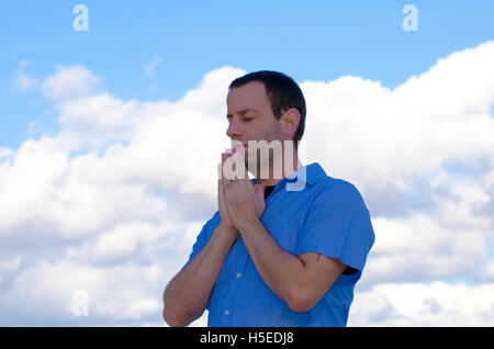 Mann, der betet mit den Wolken im Hintergrund. Stockfoto