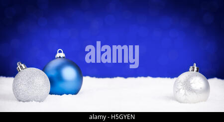 Blau und Silber Weihnachtskugeln auf Schnee mit defokussierten blauen Lichtern im Hintergrund. Geringe Schärfentiefe. Stockfoto