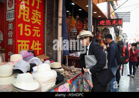 Ein chinesischer Mann versucht eine neue Mütze will er in einem Hut-Geschäft kaufen. Qibao Old Street, Beijing, China. 26.04.2016 Stockfoto