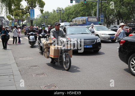 Einer chinesischen Verkehr Szene, Motorräder fahren Autos, ein Fahrer Transporte Fracht oder Pakete und Menschen Fuß zwischen den Fahrzeugen. Stockfoto