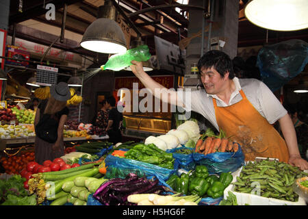 Ein Mann sprüht Wasser auf die Produkte in den bunten Obst und Gemüse Markt im Bereich Tianzifang, das ehemalige französische Viertel. Shanghai, China. Stockfoto