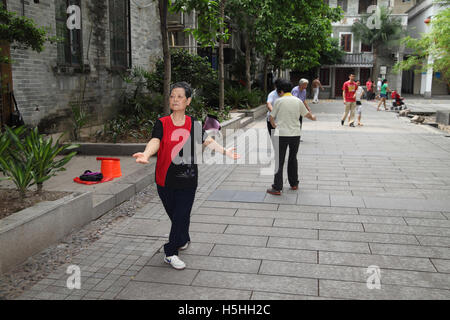 Eine ältere Frau zog und andere Menschen Tai Chi in einem öffentlichen Park zu tun, als Leute vorbei. Liwan Lake Park, Guangzhou, China. Stockfoto