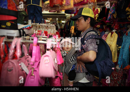 Ein chinesisches Baby sendet seine Hand, eine rosa Tasche zu berühren, während sein Vater waren in einem Kindermode Shop anschaut. Stockfoto