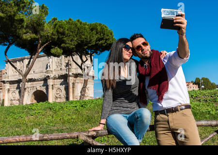 Kaukasische Pärchen nehmen ein Selbstporträt mit einem Smartphone vor dem Konstantinsbogen, Rom, Latium, Italien Stockfoto