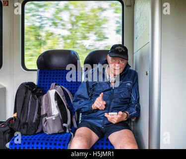 Senior Senioren Mann sitzt im Zug mit Gepäck und mit Handy Stockfoto