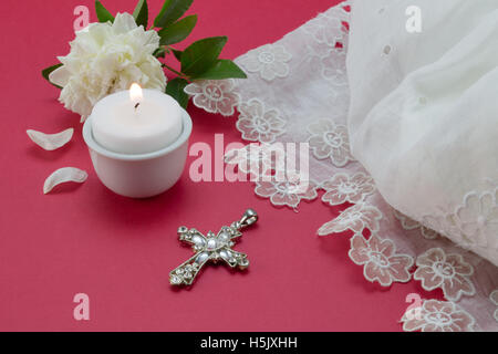 Roter Hintergrund mit weißem Vintage Spitzenkleid, Kerze und christlichen Kreuz Anhänger Taufe Stockfoto