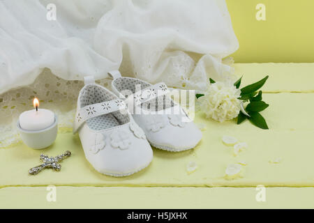 Hintergrund der Vintage Spitzenkleid Taufe auf gelben Holztisch mit Baby Booties, Kerze, Rose und Kreuz Anhänger Stockfoto