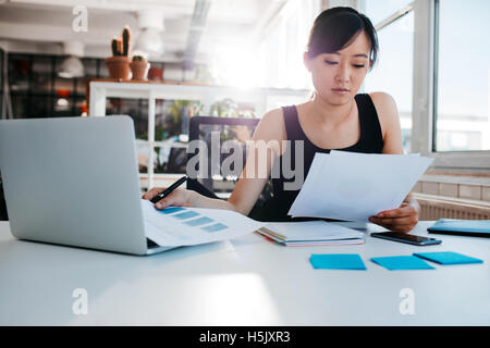 Porträt der jungen Asiatin Lesen von Dokumenten an ihrem Schreibtisch. Geschäftsfrau an ihrem Arbeitsplatz Papierkram zu tun. Stockfoto