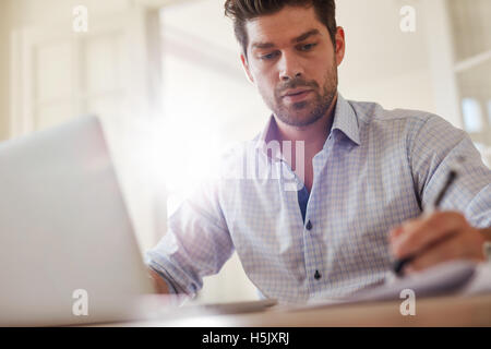 Schuss der junge Geschäftsmann Büro mit Laptop und Notizen zu Hause sitzen. Junger Mann von zu Hause aus arbeiten. Stockfoto