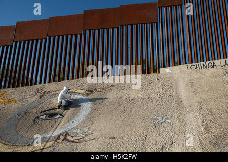 Nogales, Sonora Mexiko - ein Graffiti-Künstler malt eine Design unter der US-mexikanischen Grenzzaun. Stockfoto