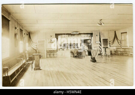 Eine echt-Photo Postkarte zeigt das Innere des scheinbar einen Versammlungsraum.  Wahrscheinlich ist das Innere des Megunticook Grange Hall.  Eine kleine Bühne mit Klavier und vier Stühlen ist hinten im Raum.  Ein Schild mit der Aufschrift "Welcome" ist über die Bühne.  Holzbänke säumen die Wände auf beiden Seiten des Raumes.   Eine amerikanische Flagge ist auf der einen Seite der Bühne.  Ein Roll – Top Schreibtisch ist in einer Ecke.  Drei Podestplätze sind mit Fahnen drapiert über sie durch den Raum eingerichtet.  Die nächste die Bühne trägt der Buchstabens "F C P."   Das Podest in der Mitte des Raumes hat ein Buch darüber. Stockfoto