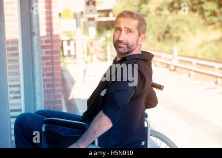 gut aussehender Mann in seinen 40ern sitzen im Rollstuhl am Bahnhof Stockfoto