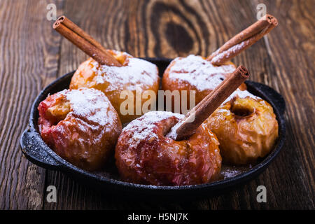Hausgemachte karamellisierte Bratäpfel mit Zimtstangen in Pfanne auf rustikalen hölzernen Hintergrund Stockfoto
