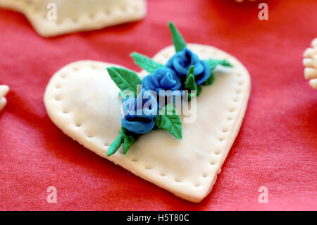 Herzförmige Kekse mit blauen Blumen auf rotem Stoff Stockfoto