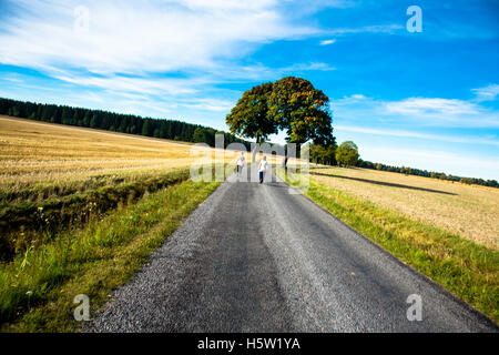 Zwei Frauen zu Fuß auf einer Straße mit den Feldern und blauem Himmel. Stockfoto