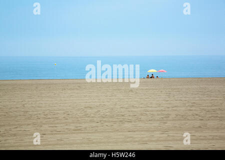 Ein paar Leute sind ganz allein am Strand und sitzen unter dem Sonnenschirm. Stockfoto