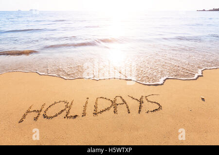 Urlaub Text im Sand von einem tropischen Strand mit hellen Sonne geschrieben Stockfoto