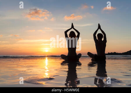 Zwei gesunde junge Erwachsene meditieren mit Yoga für Wohlbefinden am Strand bei Sonnenaufgang Stockfoto