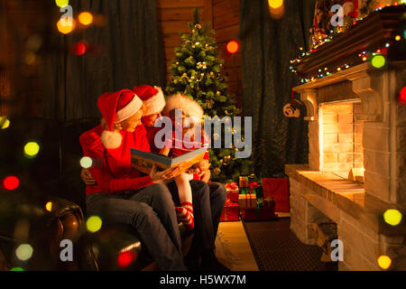 Familie lesen Sie Geschichten auf Sofa vor Kamin innen Weihnachten eingerichtetes Haus Stockfoto