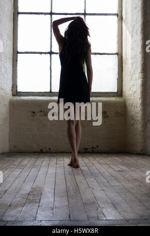 Junge Frau in kurzen schwarzen Kleid am Fenster stehend Stockfoto