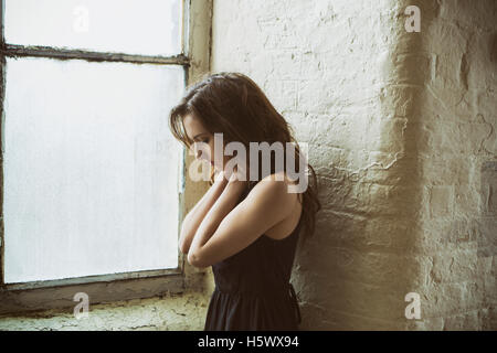 Traurige junge Frau am Fenster stehend Hände am Hals Stockfoto