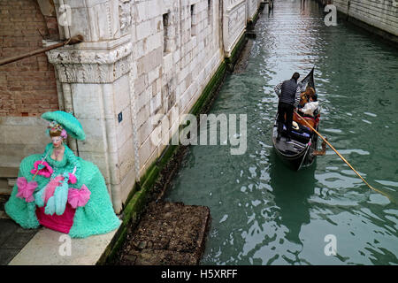 Eine maskierte Figur lehnt an einer Wand des Palazzo Ducale in Venedig, Italien, während eine Gondel vergeht Stockfoto