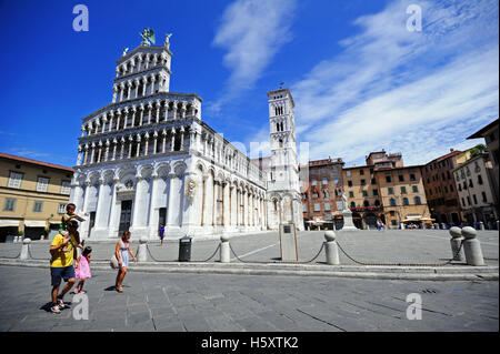 Eine junge Familie mit Kindern spaziert an der beeindruckenden Kirche San Michele in Foro, Lucca, Italien vorbei Stockfoto