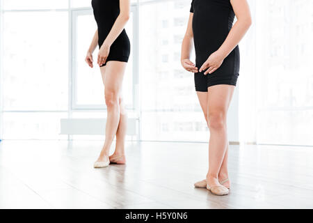 Zugeschnittenes Bild von einem jungen weiblichen Ballettlehrerin und ihr kleine knappe stehen in der gleichen Pose Ballett Stockfoto