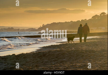 Die Atmosphäre in der Abenddämmerung wird von einem Fischer und Hund Spaziergänger am Strand von Bournemouth mit Canford Cliffs im Hintergrund genossen. Stockfoto