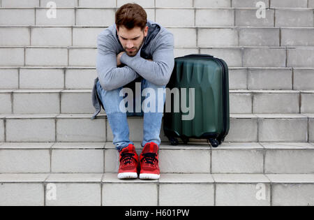 junger Mann sitzt auf Betontreppen mit Koffer Stockfoto