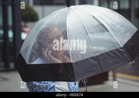 Frau mit Regenschirm beim Telefonieren mit Handy Stockfoto