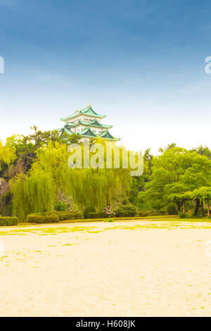 Historic Nagoya Castle Festung von außen aus der Ferne über eine grüne Baumgrenze auf einem klaren, blauen Taghimmel in Japan. Vertikal Stockfoto