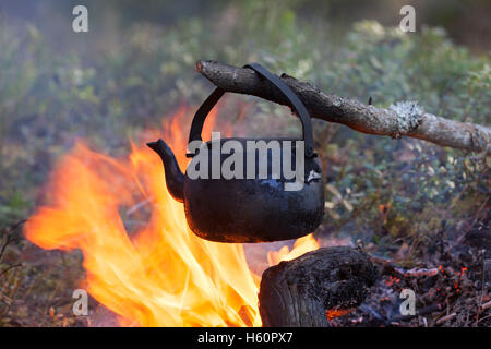 Geschwärzte Zinn Wasserkocher aus Ruß kochendes Wasser über Flammen von Lagerfeuer während der Wanderung im Wald Stockfoto