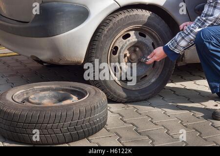 Man wandelt sich Winterreifen mit Rad Schraubenschlüssel. Vorbereitung der Wagen für den Winter. Punktierte Reifen zu reparieren. Stockfoto