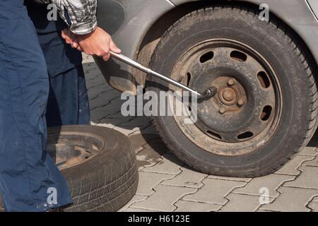 Man wandelt sich Winterreifen mit Rad Schraubenschlüssel. Vorbereitung der Wagen für den Winter. Punktierte Reifen zu reparieren. Stockfoto