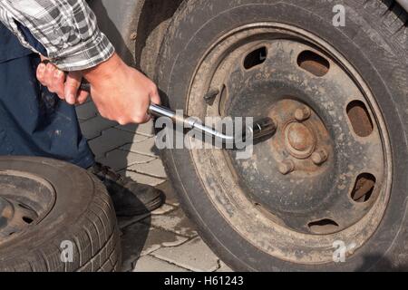 Man wandelt sich Winterreifen mit Rad Schraubenschlüssel. Vorbereitung der Wagen für den Winter. Punktierte Reifen zu reparieren. Stockfoto