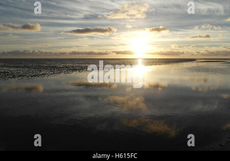 Weiße Sonneneinstellung unter grauen Stratocumulus Wolken reflektiert in einem Meer Wasser Kanal Kreuzung Ebbe Strand Sand, Fairhaven, UK Stockfoto